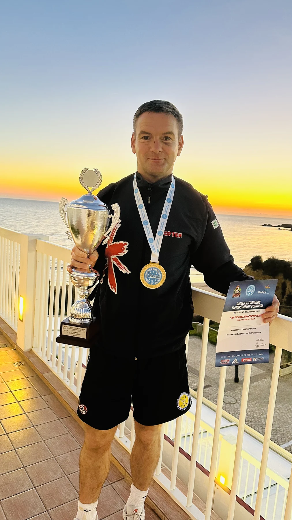 A Kickboxing competitor holding a trophy and certificate and wearing a WAKO medal