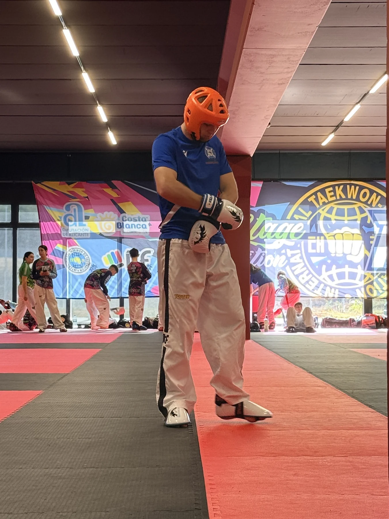 A Taekwon-Do athlete in white ITF trousers, gloves and orange headguard preparing to train